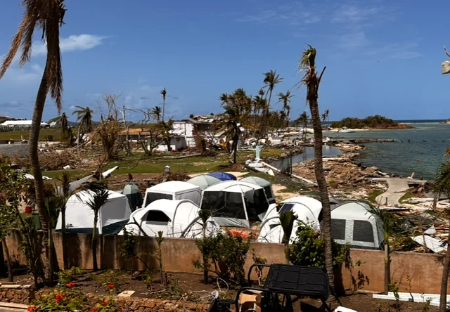 Emergency tents beside damaged buildings and palms during Union Island's post-Beryl response